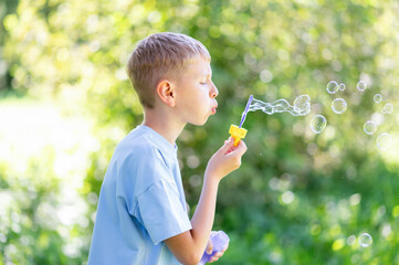 Teen boy blowing soap bubbles in summer park