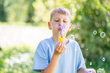 Teen boy blowing soap bubbles in summer park