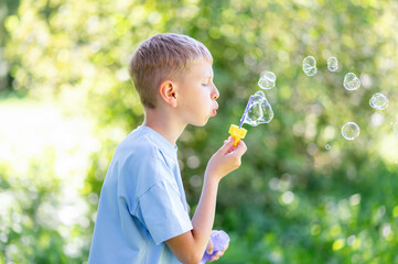 Teen boy blowing soap bubbles in summer park