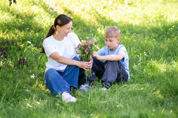 Teen boy giving mother bouquet of wildflowers on green lawn, family bonding outdoors