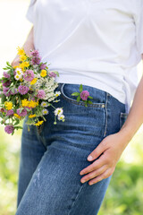 Close up of woman in blue jeans holding a bouquet of beautiful wildflowers