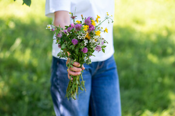 Close up of woman in blue jeans holding a bouquet of beautiful wildflowers