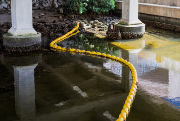 Row of bright yellow floating buoys in water under a bridge