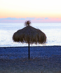 Round straw beach umbrella with wooden leg against the sea during sunset