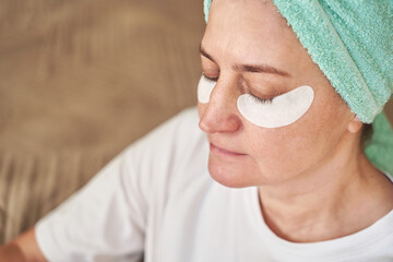 Caucasian mature female closeup with eyes closed wearing under eye patches during calm skincare...