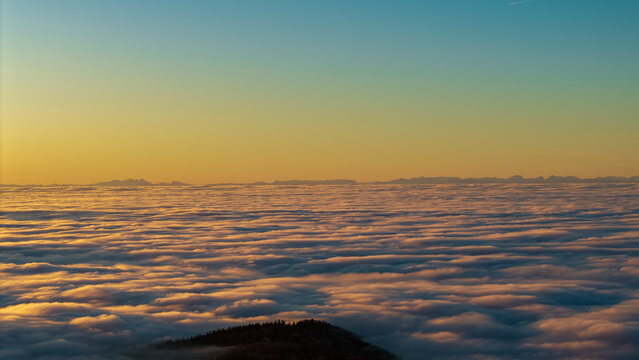Sonnenaufgang &uuml;ber einer Wolkendecke mit den Ostalpenn im Hintergrund und sanfter Beleuchtung am Morgen