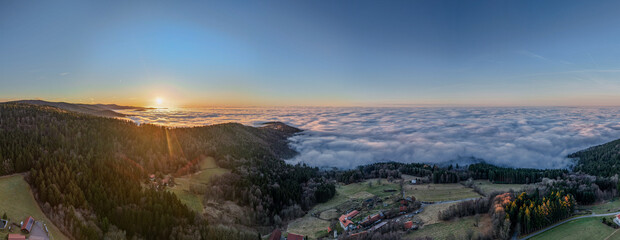 Sonnenaufgang über den Wolken in einer Berglandschaft mit Wiesen und Bäumen