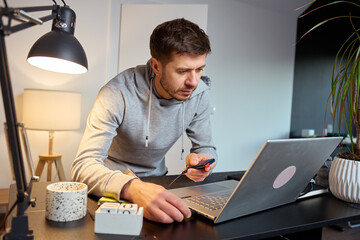 Man working with laptop and screwdriver at home office desk under lamp light