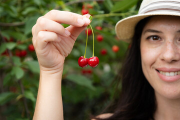 Woman smiling and proudly showing fresh ripe cherries, celebrating the abundance of a successful summer harvest season in her garden