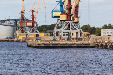 Industrial harbor with large cargo cranes along the waterfront, calm water in the foreground and port infrastructure in the background