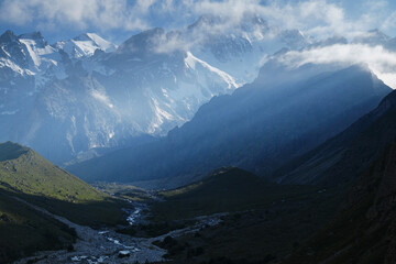 Alpine valley in the highlands with silhouettes of snow-capped mountains at dawn