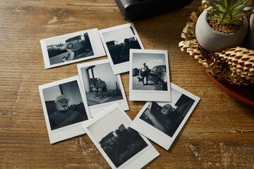 Collection of black and white photos on a wooden table showing various subjects and moments in...