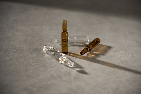 Different small glass vials of brown and clear liquid resting on a flat surface with shadows during natural light
