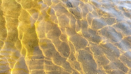 Golden sunlight reflections on clear shallow water with soft ripples and light patterns. Natural abstract background for relaxation, wellness, spa design, summer themes and calm visual projects.