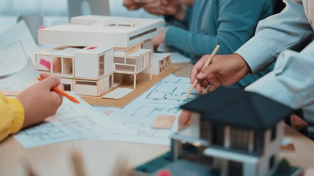 Professionals engage in a collaborative architecture design session, analyzing blueprints and a scale model in a modern office workspace, fostering creativity and teamwork. SACTR