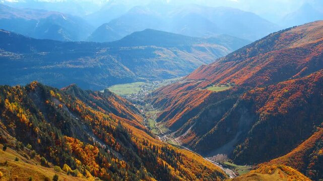 Footage over beautiful high mountains covered with plants changing color of foliage in autumn. Village in the picturesque valley at mountain foot.