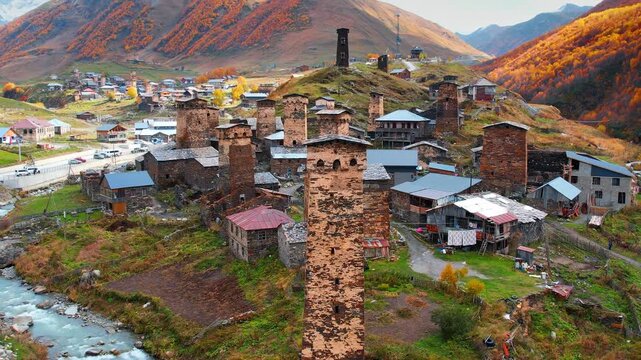 Distancing from a high tower in the medieval architecture of Ushguli, Upper Svaneti, Georgia. Orange trees in the forests cover the mountains around.