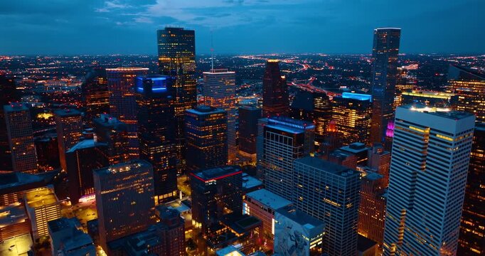 Downtown Houston, Texas, USA at night. Drone footage over the luminous cityscape. Revealing view on the intertwining highways with lively traffic at backdrop.