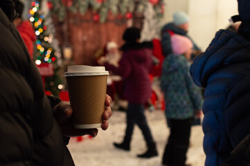 Person Holding Hot Coffee at Christmas Market. Cozy Winter Scene with Coffee Cup and Festive Background