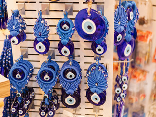 Various blue talismans hang from a display in a shop. The items include beads and amulets featuring an eye design. Shoppers browse the colorful selections