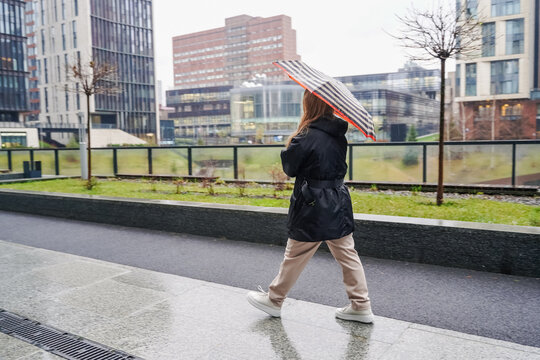 Crossing pedestrian carries umbrella on rainy urban sidewalk. Moving along wet pavement with city commute vibe. Travel lifestyle, street scene, bad weather protection, waterproof canopy. Transport.