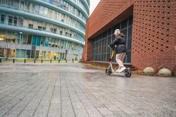 Accelerating electric scooter across wet plaza during city commute rush hour. Pushing micromobility transport through rainy weather. Travel movement for urban lifestyle with scooter ride speed.