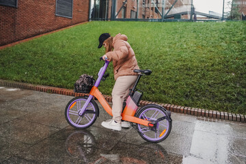 Steering rented electric bicycle through rain on wet pavement during commute. Cycling movement boosts fitness, exercise. Ebike rental sharing supports sustainable mobility, last mile travel.