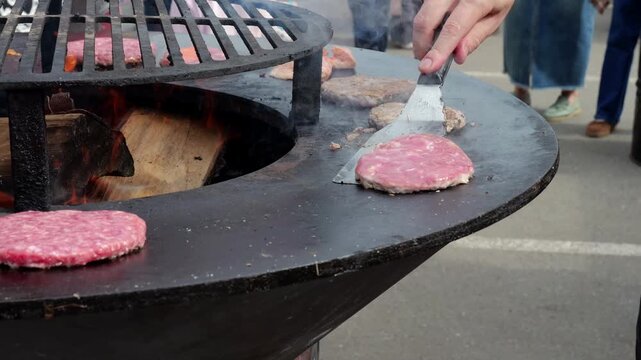Open flame grilling, Street food vendors flipping burgers with lively crowd nearby, Festival scene featuring sizzling burgers on open grills surrounded by excited
