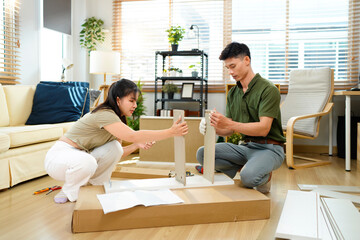 Asian adult couple assembling wooden furniture together in modern living room create new home decor DIY project happiness