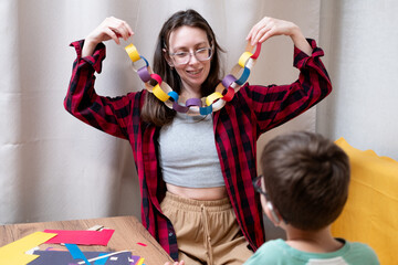 A young woman in a red plaid shirt makes a paper garland for Christmas with her son, who uses hearing aids. DIY Christmas home decor.
