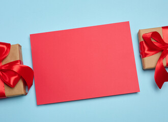 A red, blank rectangular sheet of paper between two craft-wrapped gift boxes with red satin bows.