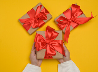 A woman's hands in a white knitted sweater hold a gift box with a red satin bow.