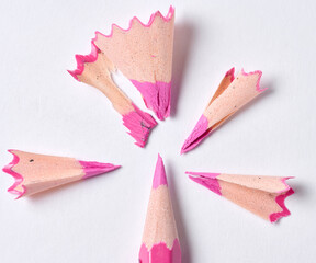 Wooden shavings and pink pencil on white background, top view