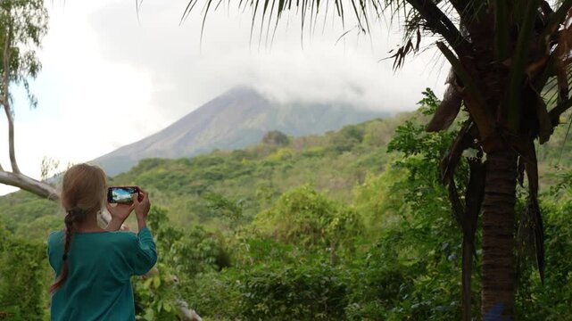 A mature woman hikes through Charco Verde park on Ometepe Island in Nicaragua while taking pictures of the volcano and surrounding nature.