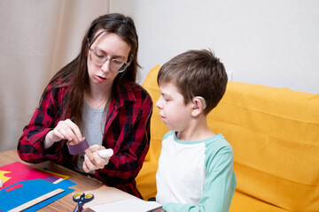 A young woman in a red plaid shirt and her son with hearing aids glue together a paper garland for Christmas. DIY Christmas home decor.