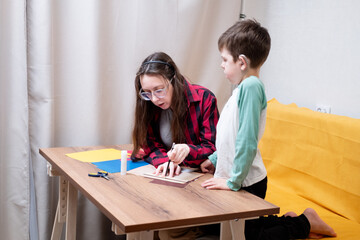 A young woman in a red plaid shirt and her son, who uses hearing aids, draw on construction paper to make a paper garland for Christmas. DIY Christmas home decor.