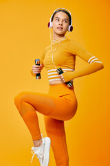Female fitness model in bright orange activewear holding small dumbbells and wearing headphones,...