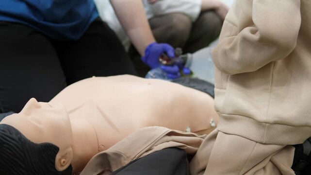 bag valve mask ventilation on adult mannequin during team training, gloved trainees coordinate chest compressions and manual ventilation with ambu bag, instructor guides technique, emergency