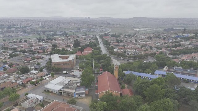 Drone orbits to the left around plaza with Hector Pieterson Memorial and Holy Cross Church on rainy day in Soweto, South Africa