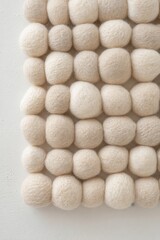 Soft wool felt balls in beige and white colors arranged in a grid pattern.