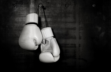 White leather boxing gloves hanging on black wall