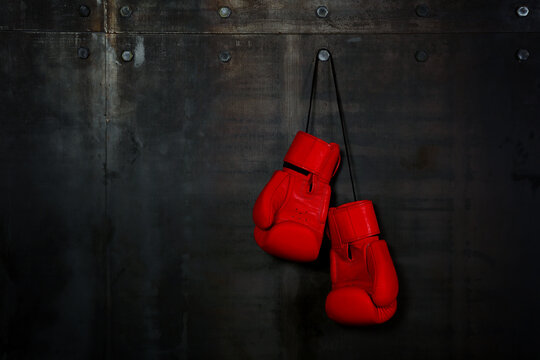 Red leather boxing gloves hanging on black wall