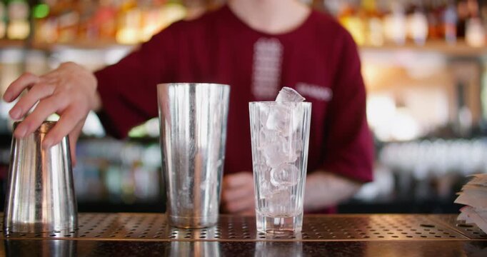 Cocktail bar. Preparing cold drink. Barkeeper adding ice cubes to metal shaker. Professional mixologist making refreshing beverage in cafeteria.