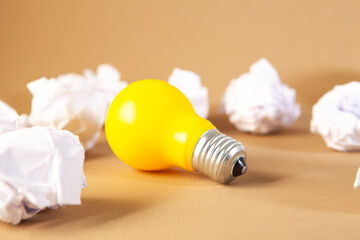 Light bulb with crumpled paper balls on a brown background.
