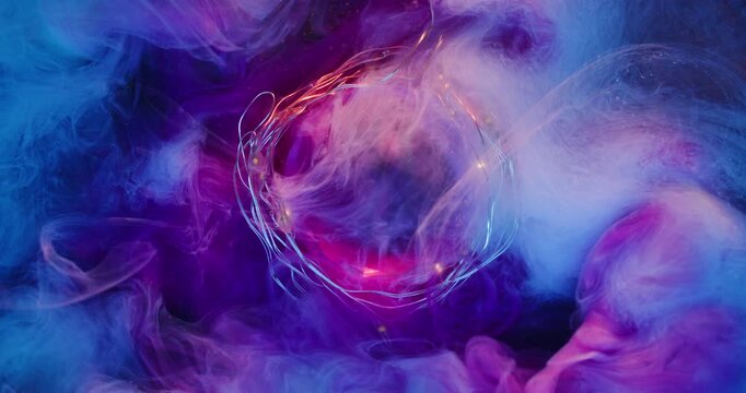 Ink shot. Defocused fume wave. Pink mist color dye spray in blue liquid. Smoke pigment mix on round frame light garland abstract purple background.
