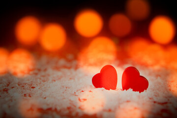 Two red hearts in the snow with bokeh lights on background