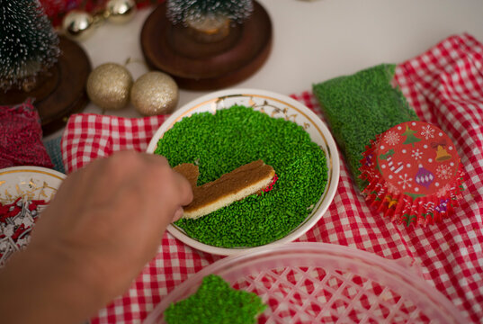 Mano de mujer sostiene un galleta en forma de baston y  la decora con filigranas navide&ntilde;as