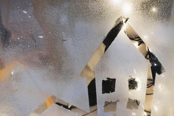 Weihnachtsdekoration an Schneebedecktem Fenster mit Licht und ausgeschnittenem Haus mit Spitzdach