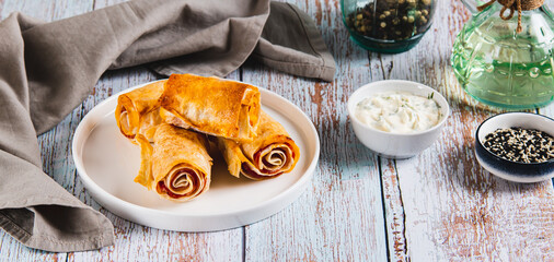 Mini rolls of lavash, bacon and cheese on a plate on the table web banner