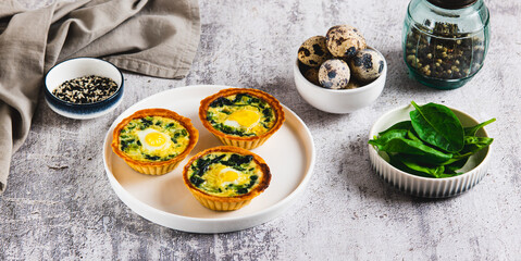 Baked tartlets with quail eggs and fresh spinach on a plate on the table web banner